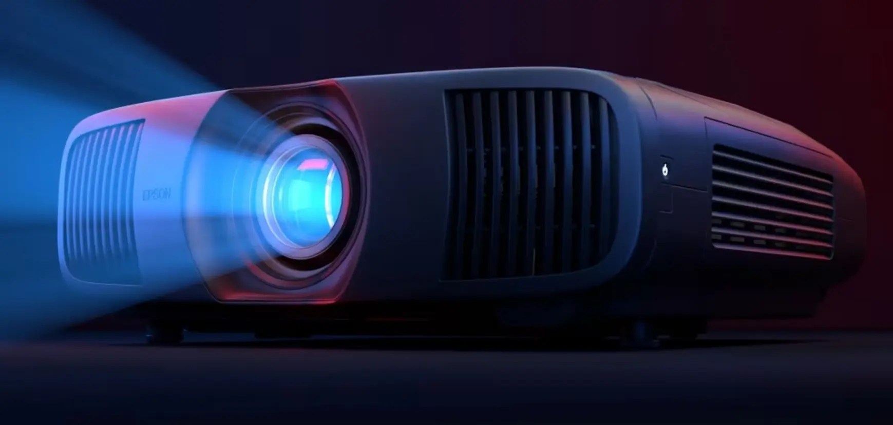 Epson EH-LS9000 Epson EH-LS9000 visto de frente, con luz azul saliendo del lente y ventilación visible a la derecha.